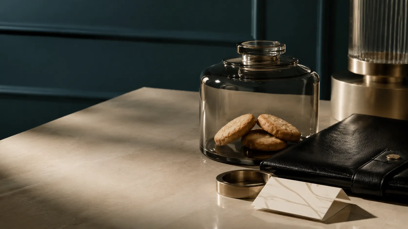 A glass jar containing biscuits beside a black leather folio and brass desk accessories.